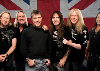 Skupinová fotografia členov kapely Iron Maiden stojacich pred britskou vlajkou.