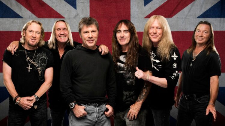 Skupinová fotografia členov kapely Iron Maiden stojacich pred britskou vlajkou.