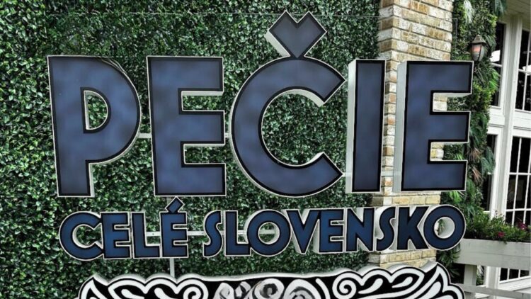 Logo relácie „Pečie celé Slovensko“ na pozadí zelenej steny s nápisom v modrej farbe.