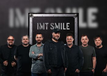 IMT SMILE stojí pred pódiovou kulisou s logom skupiny, pripravená osláviť 20. výročie albumu Exotica novým live albumom Exotica Live 2004.