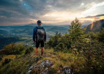 Turista stojí na vrchole kopca pri západe slnka, s výhľadom na malebnú slovenskú krajinu.