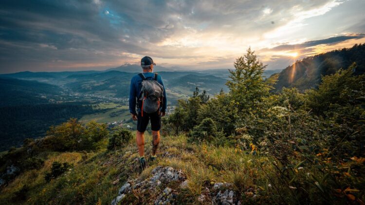 Turista stojí na vrchole kopca pri západe slnka, s výhľadom na malebnú slovenskú krajinu.