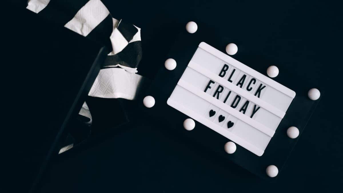 Svetelná tabuľa s nápisom "Black Friday" a srdiečkami, vedľa otvorenej darčekovej krabičky na čiernom pozadí.