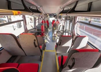 Interiér moderného autobusu s červenými a šedými sedadlami, pripravený na cestujúcich.