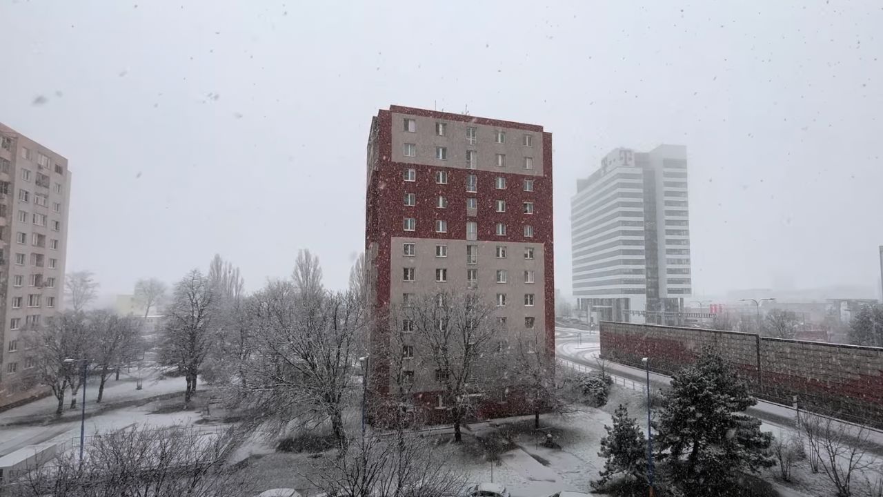 Sneženie na križovatke Bajkalská a Prievozská v Bratislave, zasnežené stromy a budovy počas zimnej atmosféry.