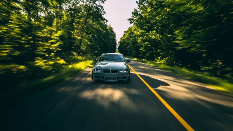 Auto na ceste obklopenej stromami, ktoré vytvárajú zelenú scenériu, zachytené počas jazdy.