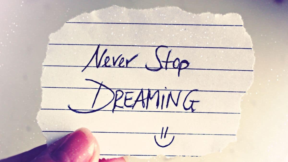 Ručne napísaný citát „Never stop dreaming“ na roztrhanom kúsku papieru, držiacom v ruke, s jemným trblietavým efektom na pozadí.