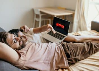 Muž a žena ležia na posteli a sledujú Netflix na notebooku v pohodovej atmosfére.