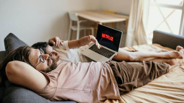 Muž a žena ležia na posteli a sledujú Netflix na notebooku v pohodovej atmosfére.