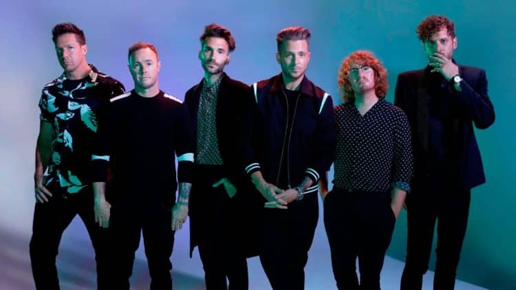 Členovia kapely OneRepublic na promo fotografii s moderným osvetlením a štýlovým outfitom.