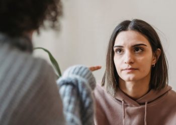 Žena vyzerá neisto a smutne, zatiaľ čo druhá osoba na ňu ukazuje prstom v hádke.